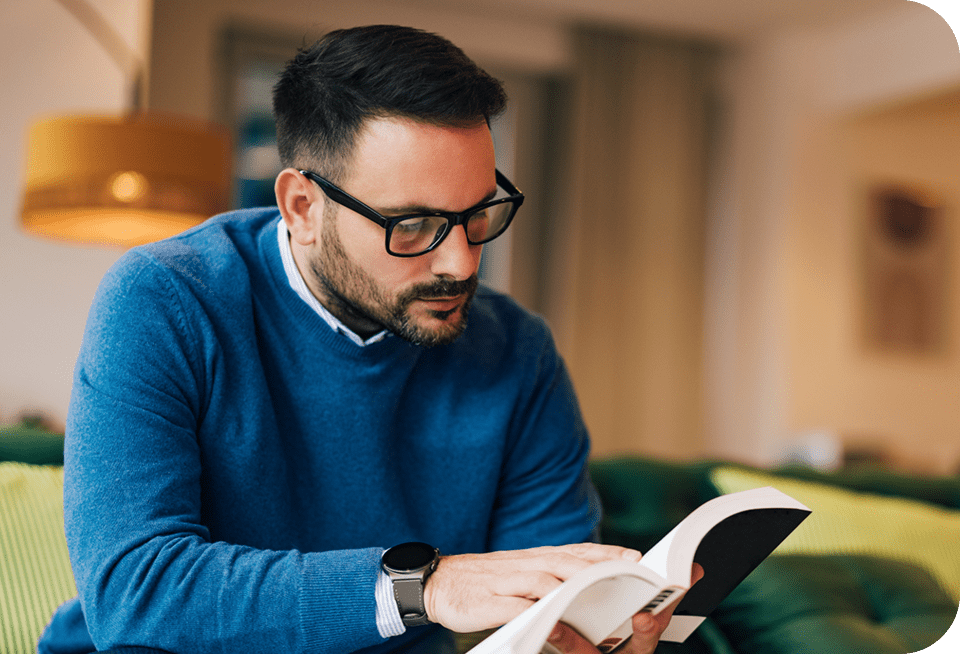 Man wearing glasses reading a book indoors.
